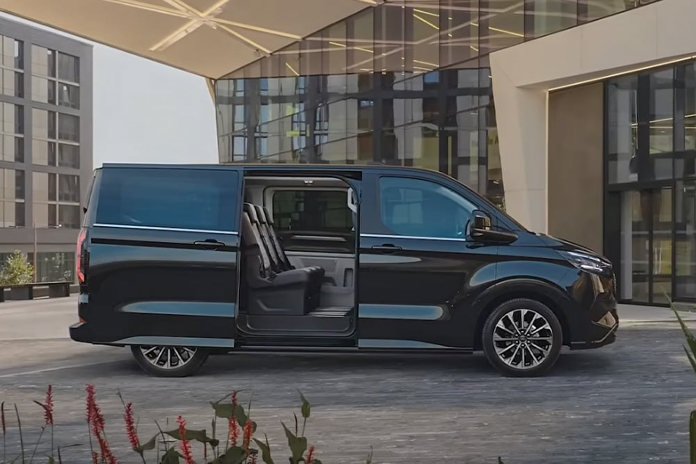 Een zwarte Ford E-Tourneo Custom staat geparkeerd met de zijdeur open, waardoor de interieurstoelen zichtbaar zijn.