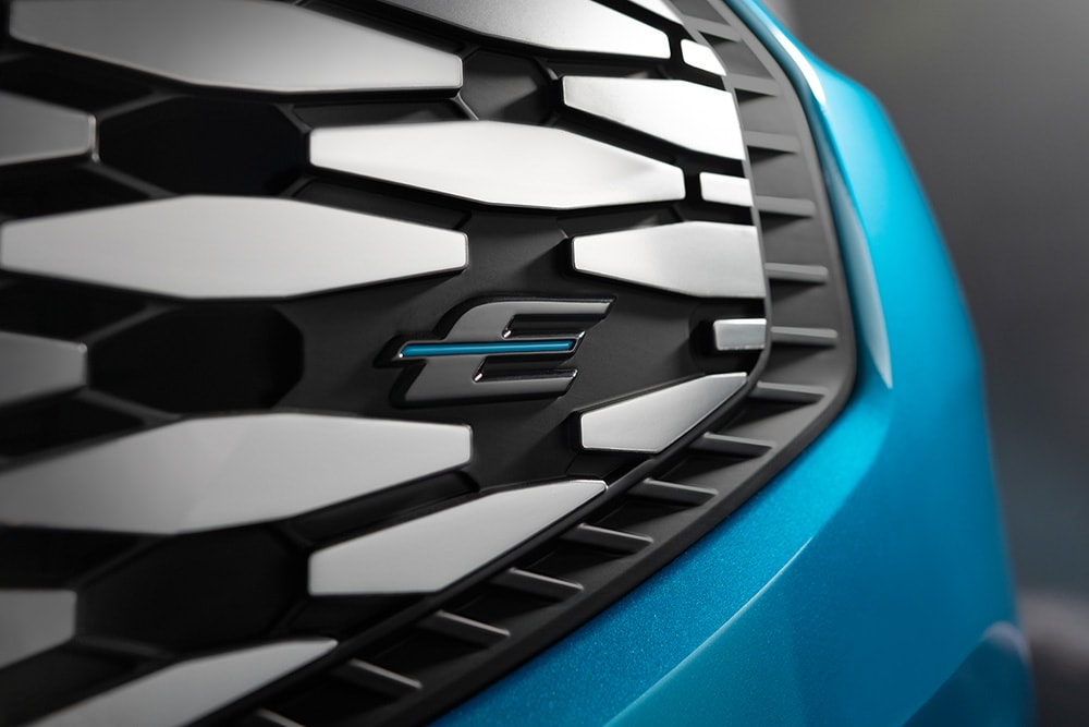 Close-up van de grille van de Ford E-Tourneo Custom, met het blauwe "E"-logo, exclusief voor elektrische Ford-modellen.