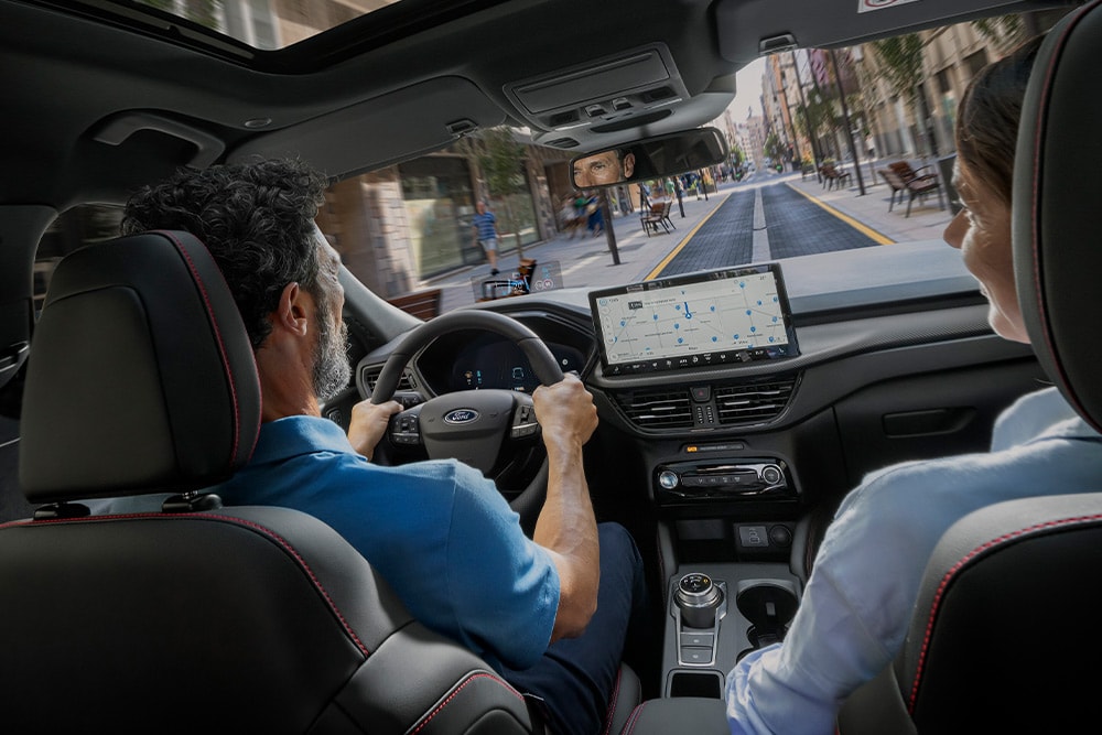 Twee personen rijden in een  Ford Kuga door de stad met behulp van de aanwijzingen op het 12,3" digitale display.