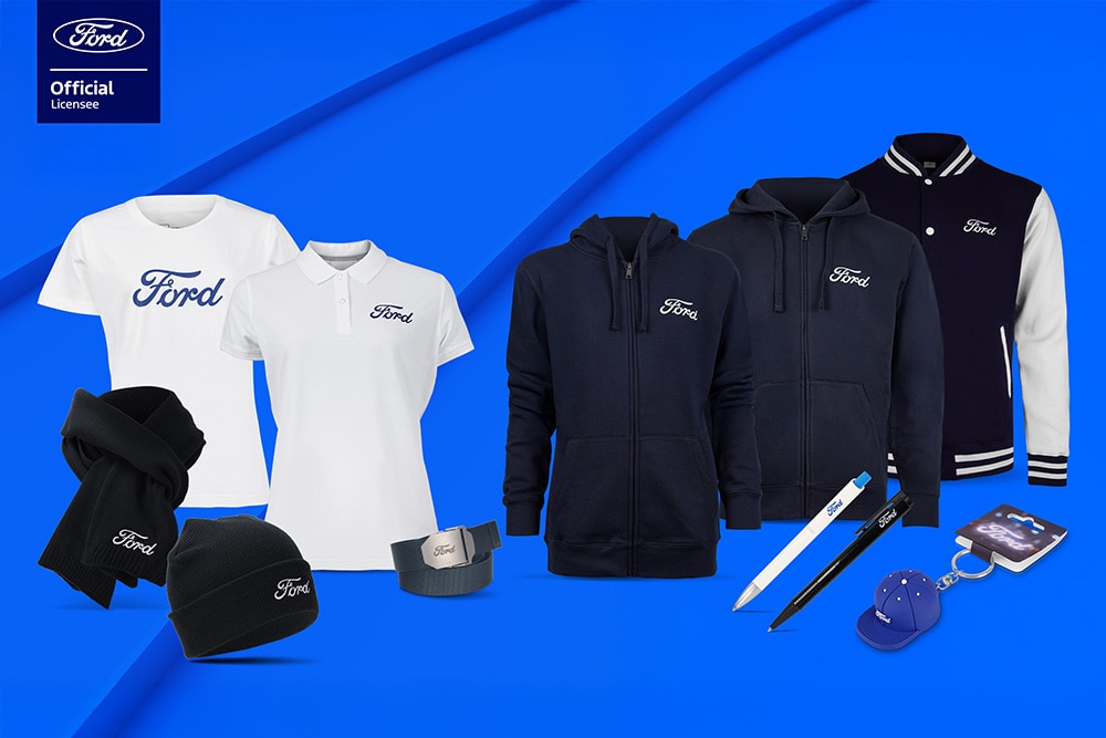 Ford merchandise collectie met paraplu, mokken en kleding, met diverse Ford voertuigen op de achtergrond. 