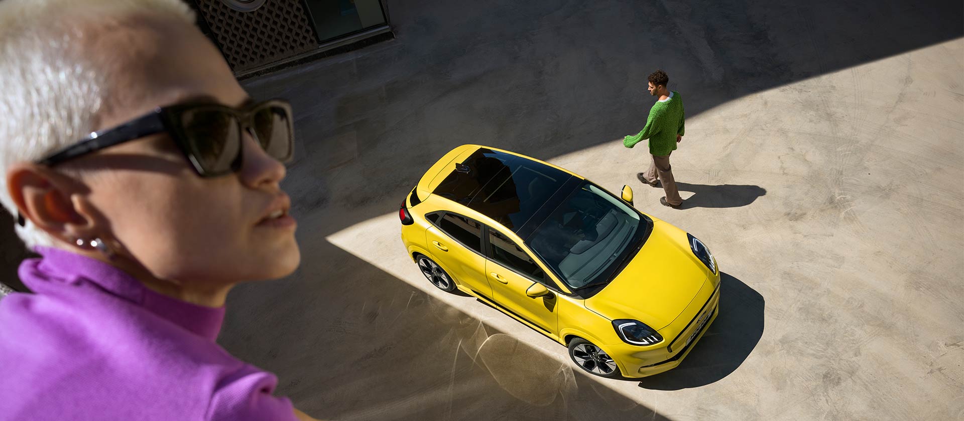 Vogelperspectief van een gele elektrische Ford Puma Gen-E®. Persoon in het paars op de voorgrond.
