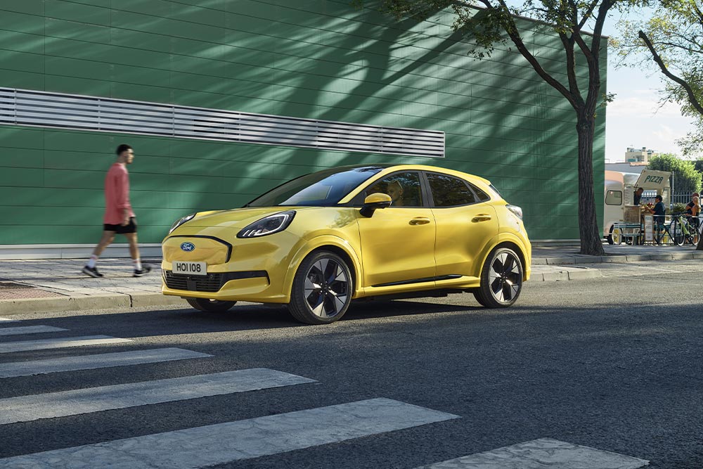 Zijaanzicht van een gele elektrische Ford Puma Gen-E® geparkeerd langs de kant van de weg.