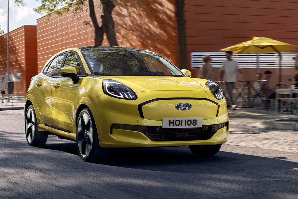 Vooraanzicht van een gele elektrische Ford Puma Gen-E® die op een stadsweg rijdt.