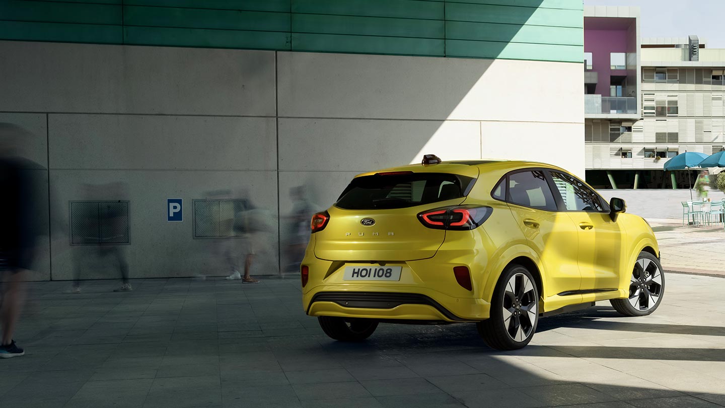 De achterkant van een gele elektrische Ford Puma Gen-E® geparkeerd onder een brug.