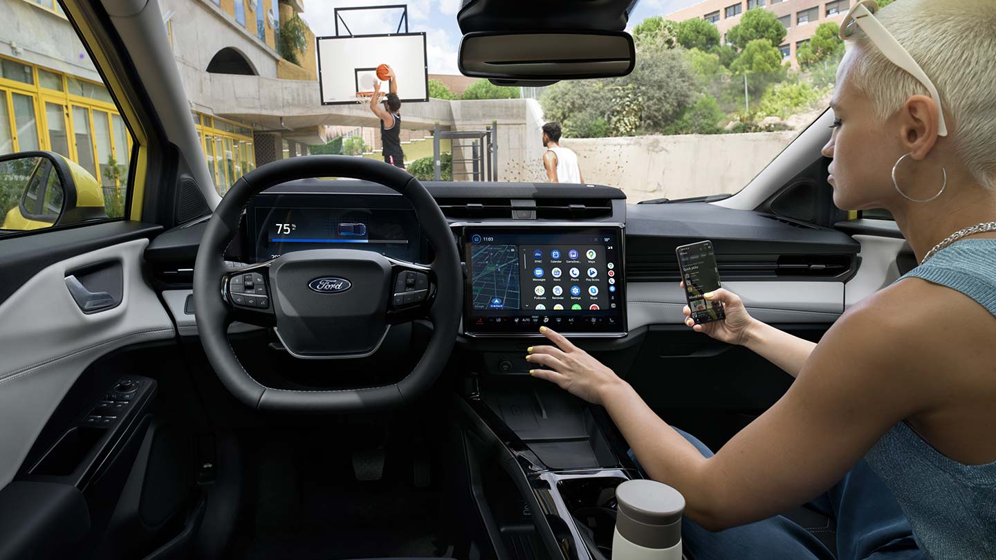 Het interieur van de elektrische Ford Puma Gen-E®, terwijl iemand zijn mobiel draadloos synchroniseert met het touchscreen.