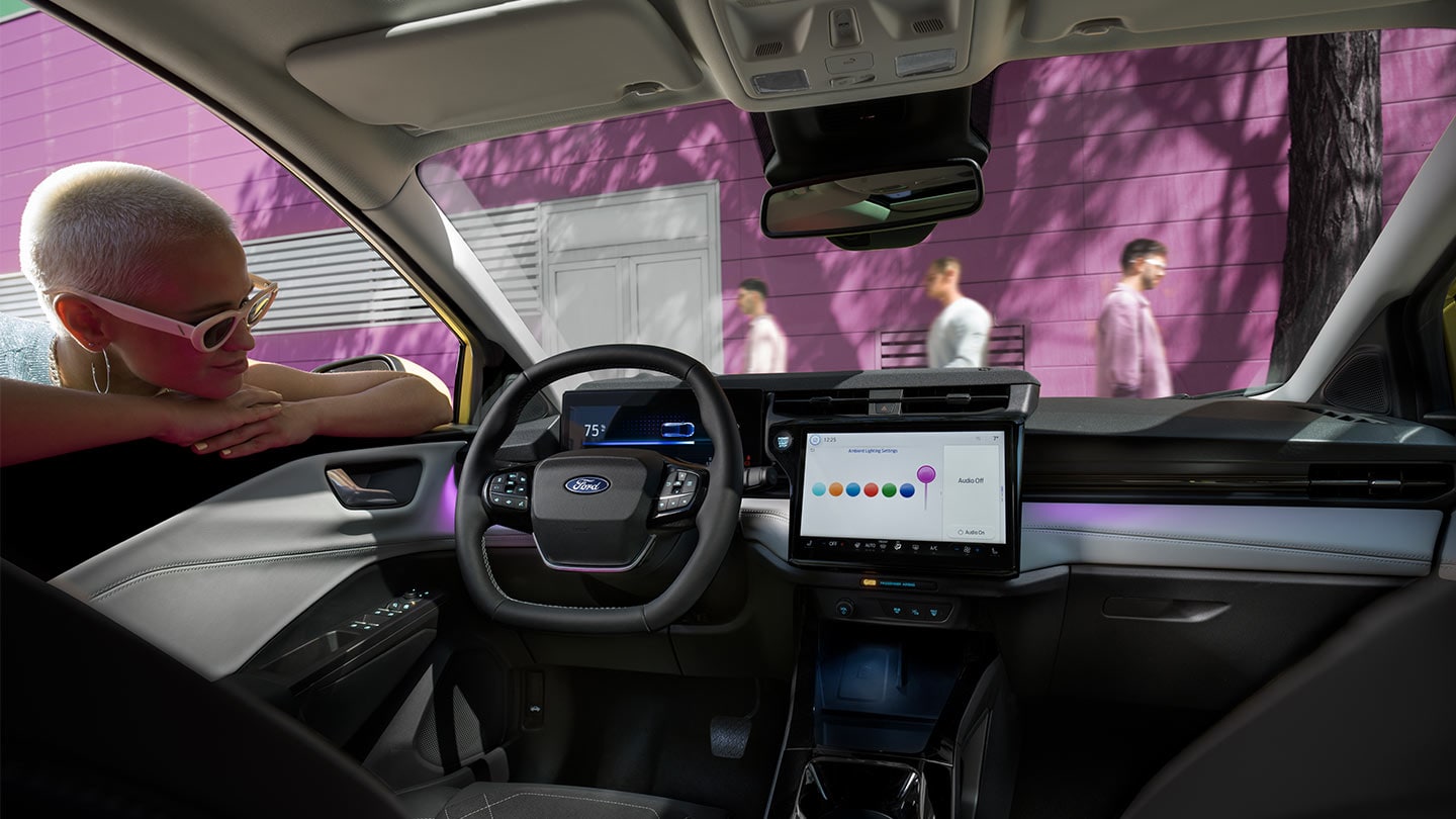 Persoon die kijkt naar het interieur van de nieuwe Ford Puma Gen-E®, met een groot touchscreen en binnenverlichting.