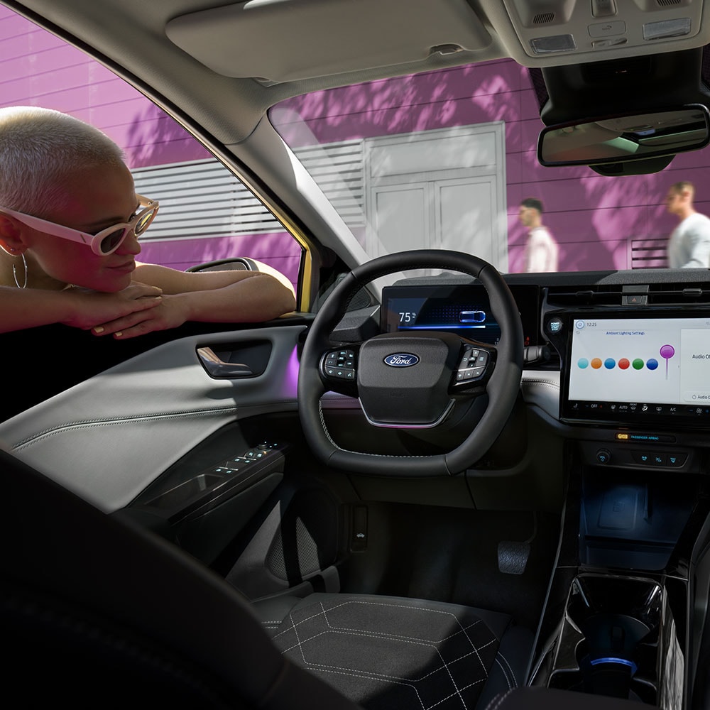 Het interieur van de elektrische Ford Puma Gen-E®, met iemand die door het raam naar het grote infotainmentscherm kijkt.