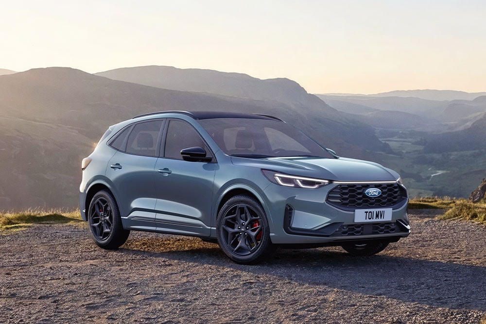 Een grijze Ford Kuga die geparkeerd staat op een onverharde bergweg bij zonsondergang.