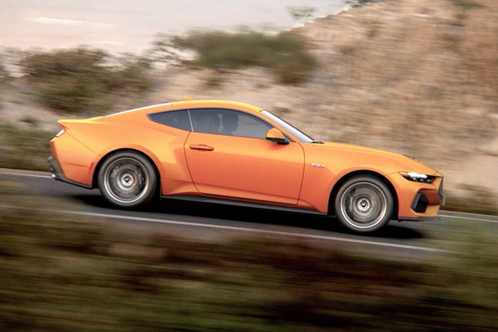 Zijaanzicht van de Ford Mustang GT Fastback in Orange Fury die over een weg rijdt