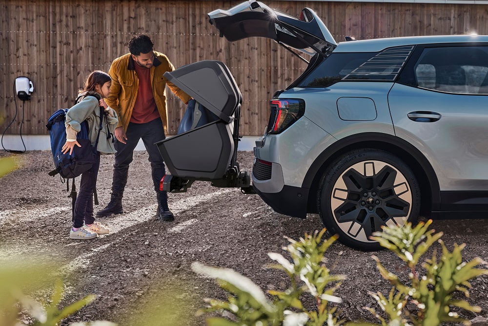 Een man en kind die bij de open kofferbak van een Ford Explorer SUV staan en een opgevouwen kinderwagen in de kofferbak doen.