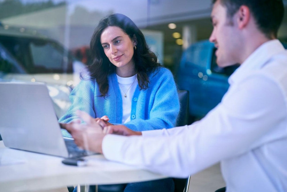 Een klant in een blauwe vest bespreekt opties op een laptop met een showroommedewerker.