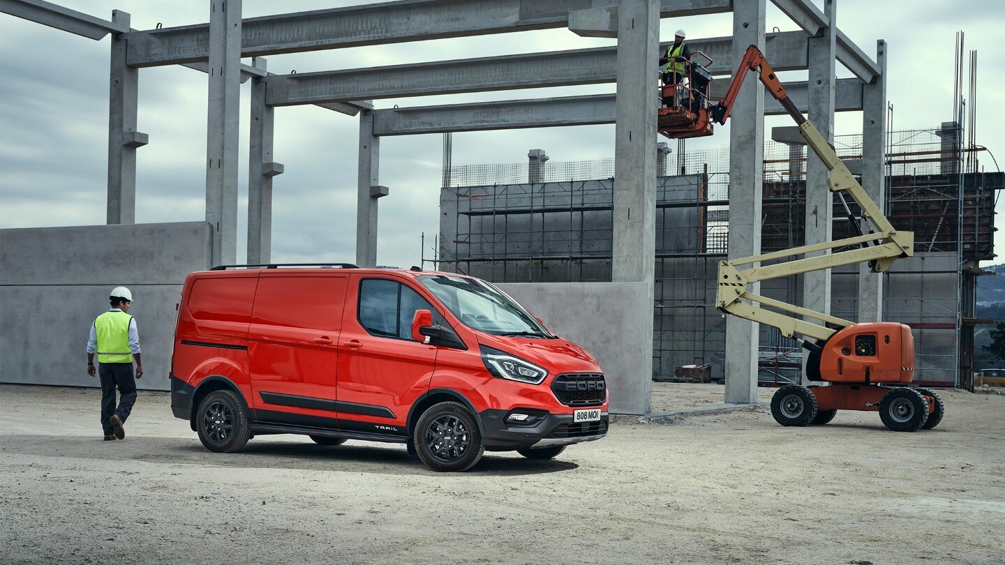 Rode Ford Transit Custom Trail geparkeerd voor een gebouw in aanbouw