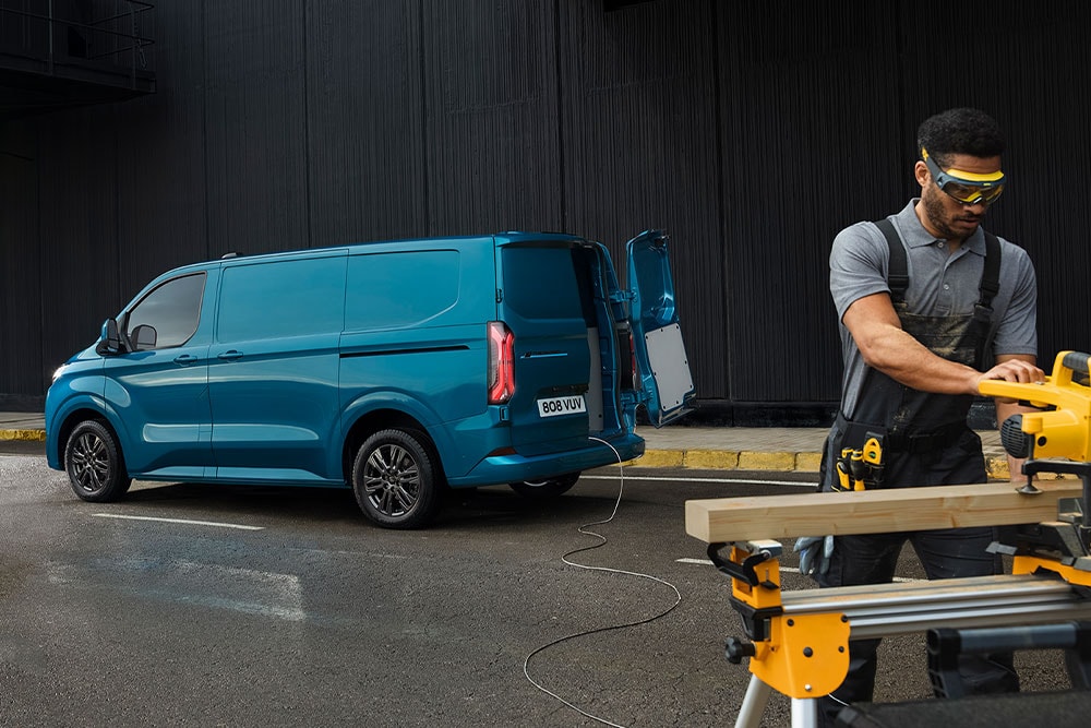 Blauwe Ford E-Transit Custom elektrische bestelbus en iemand die elektrisch gereedschap gebruikt.