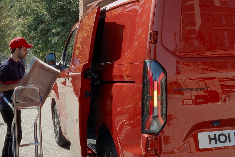 Een bezorger laadt pakketten uit een rode Ford Transit Custom.