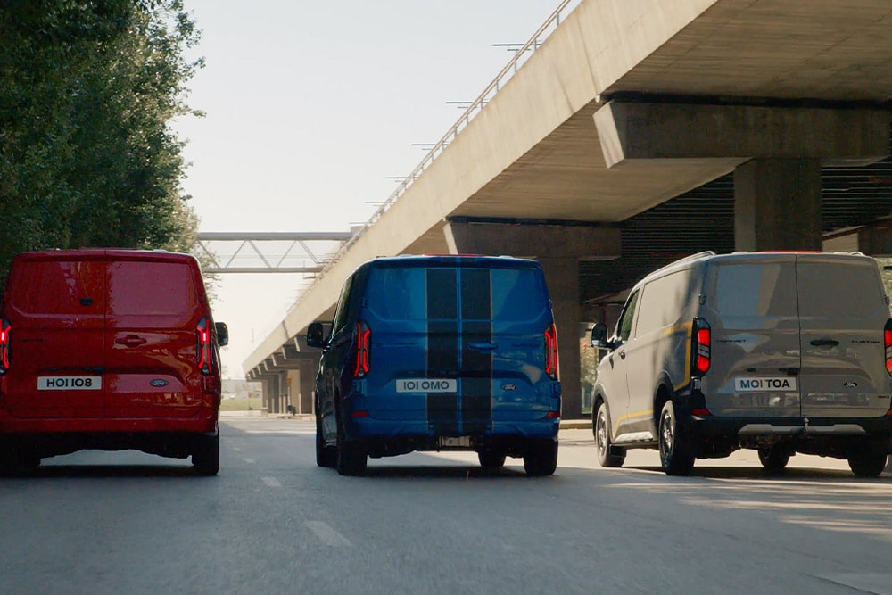 Drie geparkeerde Ford Transit Custom Sport-bestelwagens in het grijs, blauw en rood.