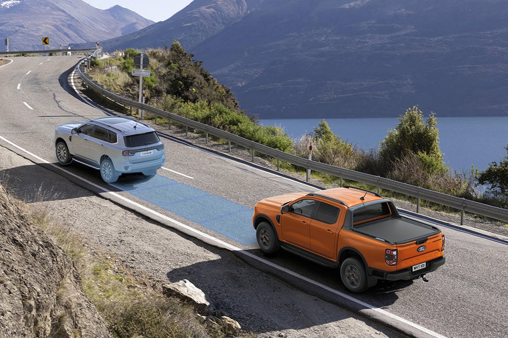 Een gele Ford Ranger Raptor rijdt over een schilderachtige bergweg, met nadruk op de rijhulpsystemen van het voertuig.