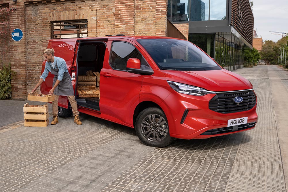 Een bezorger laadt pakketten in via de zijdeur van een rode Ford Transit Custom.