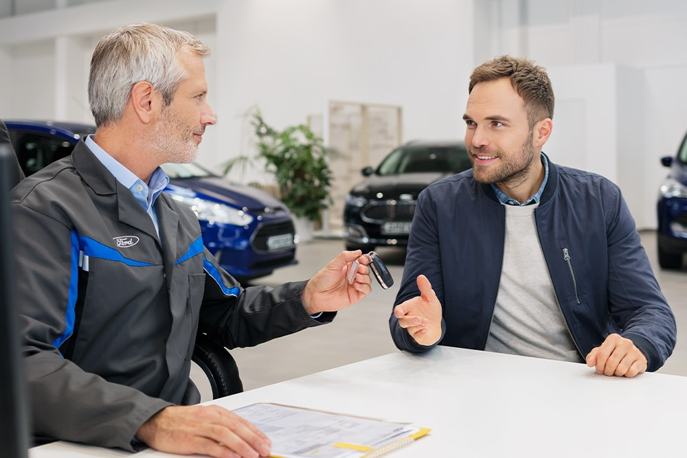 Een Ford-adviseur overhandigt sleutels aan een klant tijdens een gesprek over de verschillende Ford-financieringsopties.