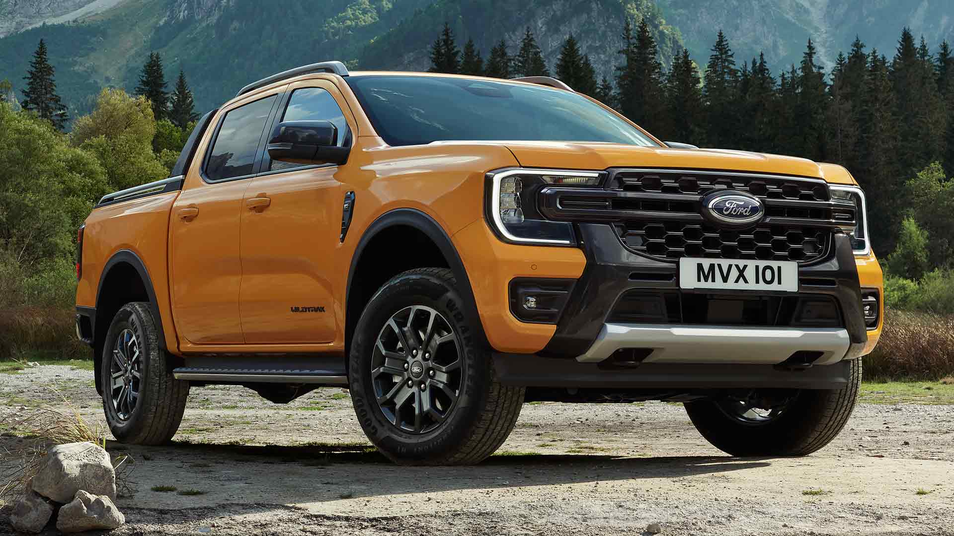 Een gele Ford Ranger Wildtrak met dubbele cabine met een sfeervol bos en bergen op de achtergrond.