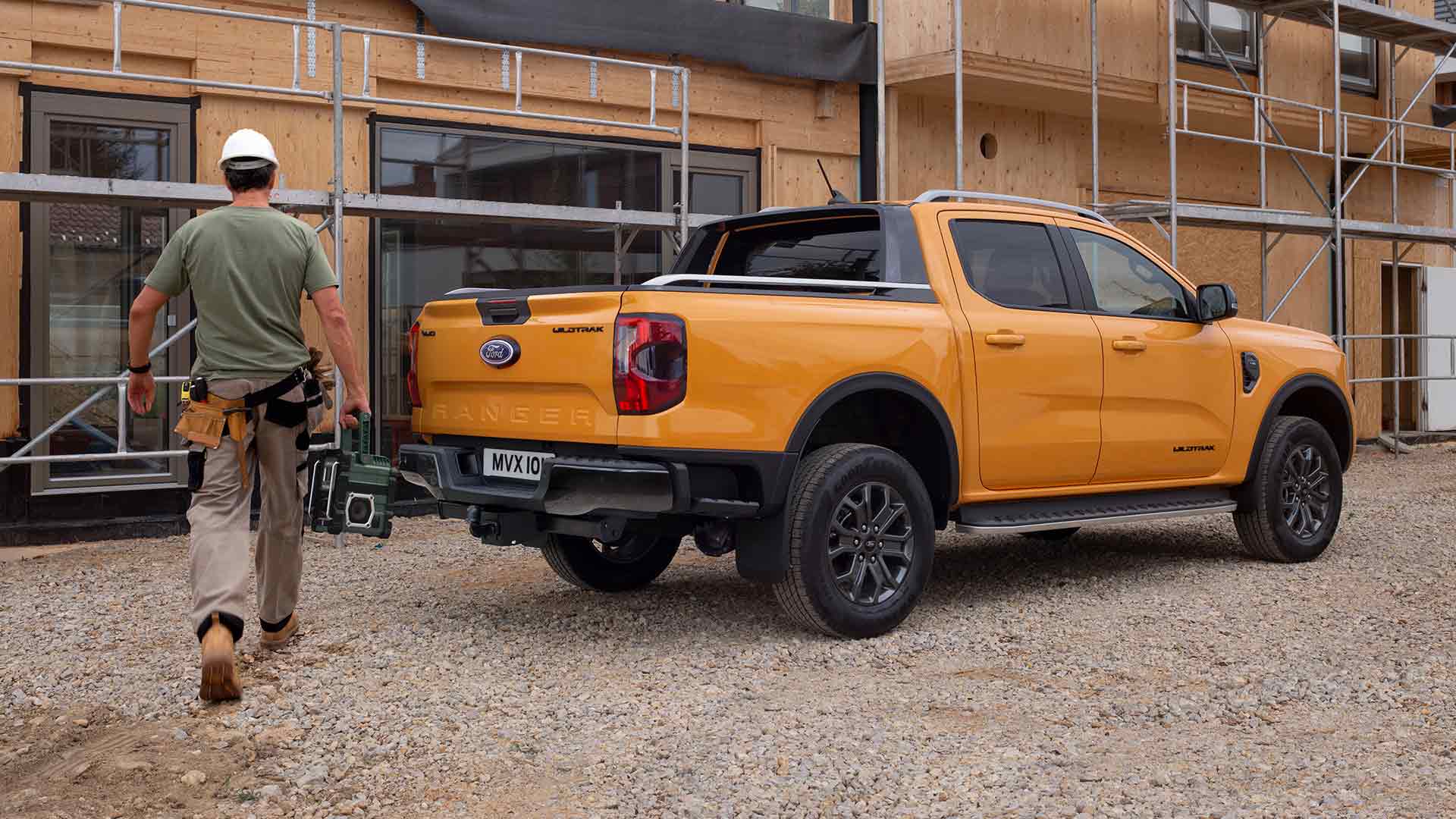 Driekwart achteraanzicht van een gele Ford Ranger Wildtrak met dubbele cabine op een bouwplaats.
