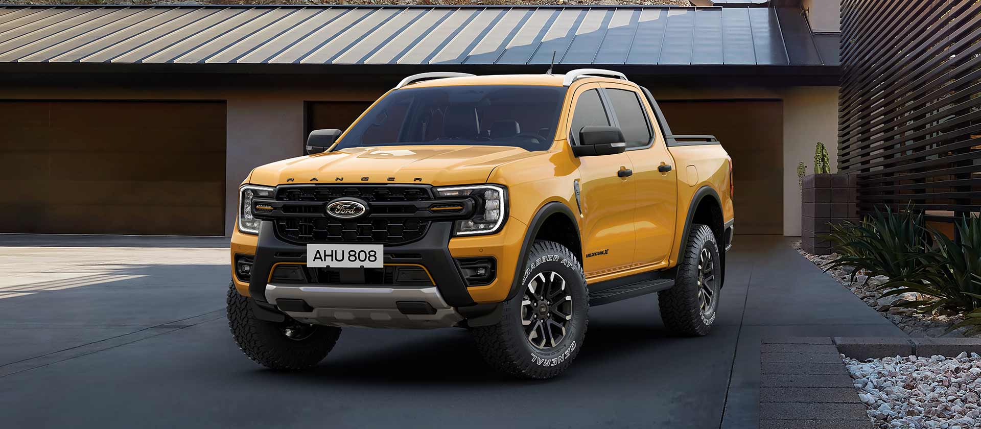 Een gele Ford Ranger met dubbele cabine, geparkeerd voor een huis.