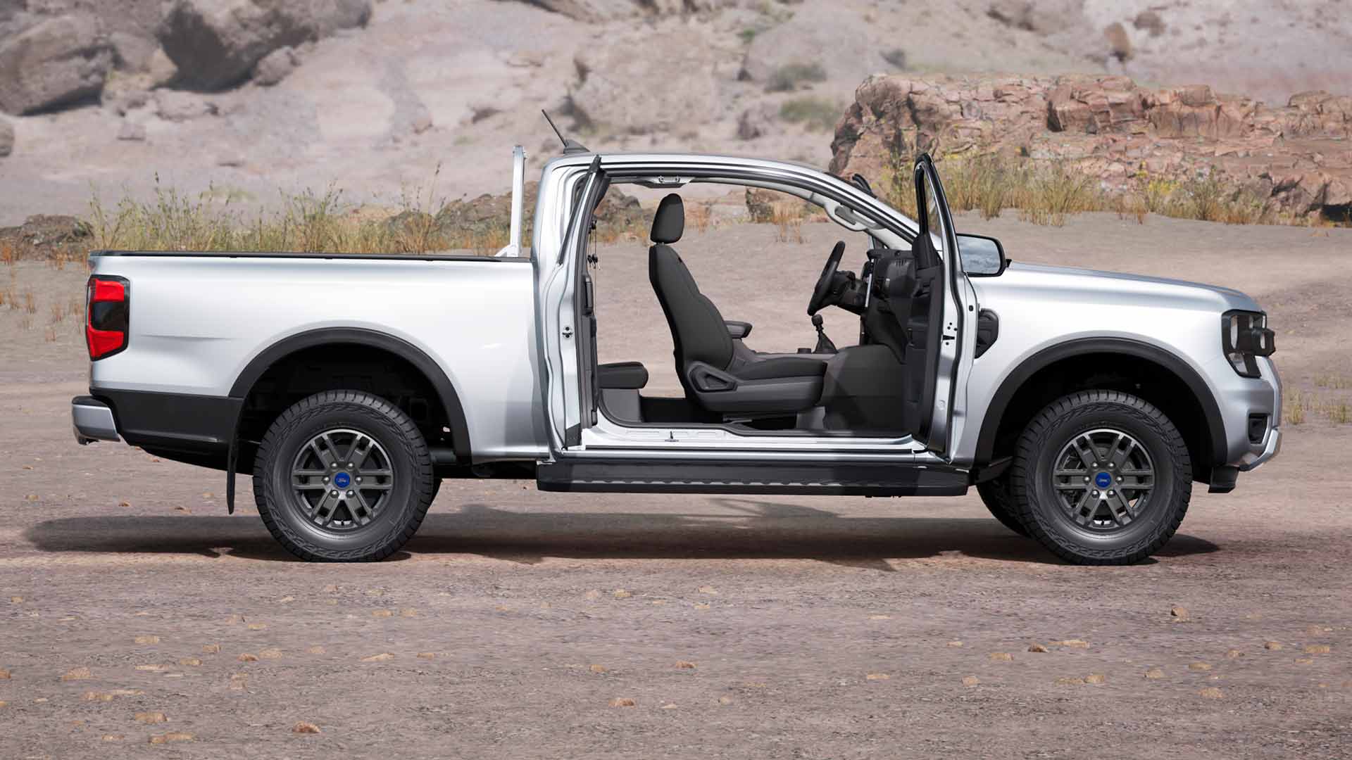 Profiel van een zilveren Ford Ranger XLT met supercabine met open deuren, geparkeerd in een stoffig gebied.