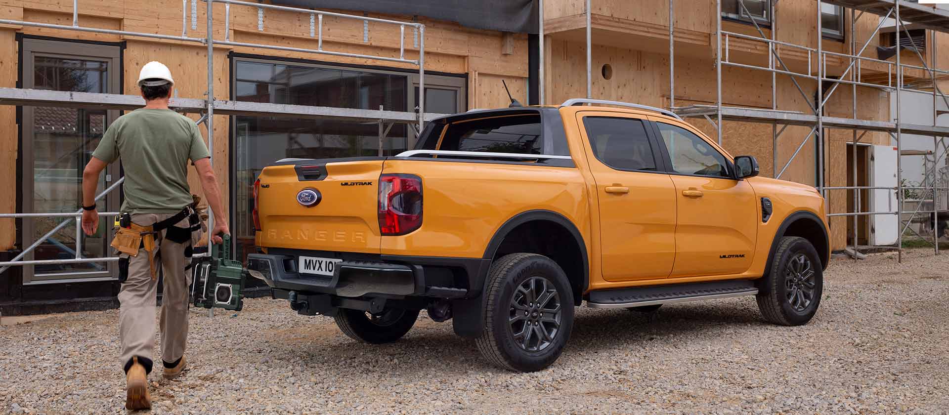 Een bouwvakker met een helm loopt op een bouwplaats naar een gele Ford Ranger pick-uptruck.
