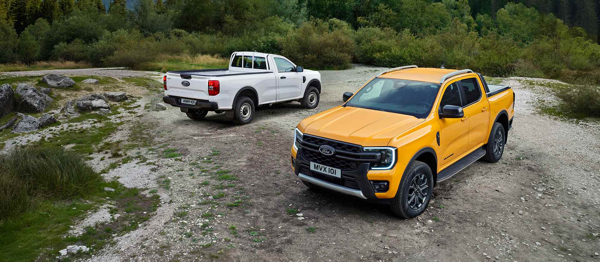 Een witte Ford Ranger en een gele Ford Ranger staan geparkeerd aan een rotsachtige kant van de weg. 