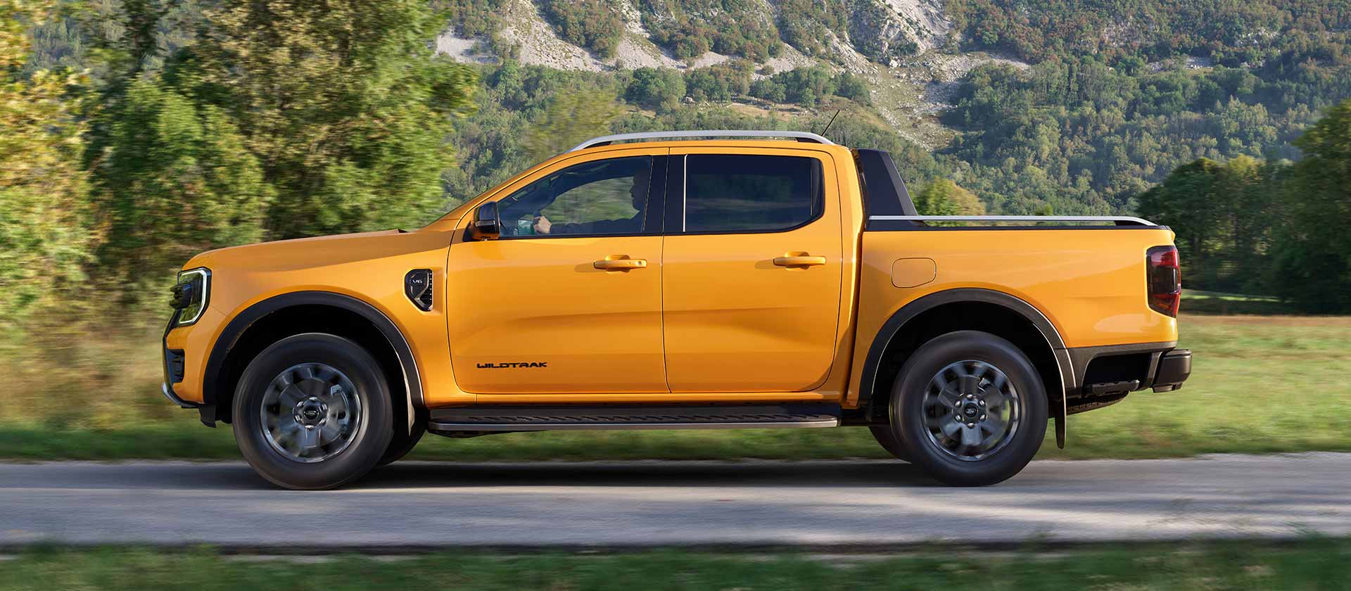 Zijaanzicht van een gele Ford Ranger Wildtrak die op een verharde weg rijdt.