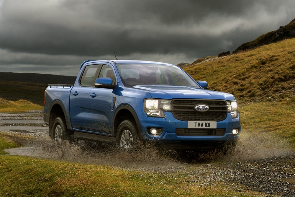 Een blauwe Ford Ranger waadt door een ruig landschap.