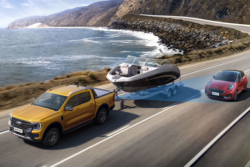 Een gele Ford Ranger sleept een boot langs een kustweg en laat zijn trekvermogen zien.
