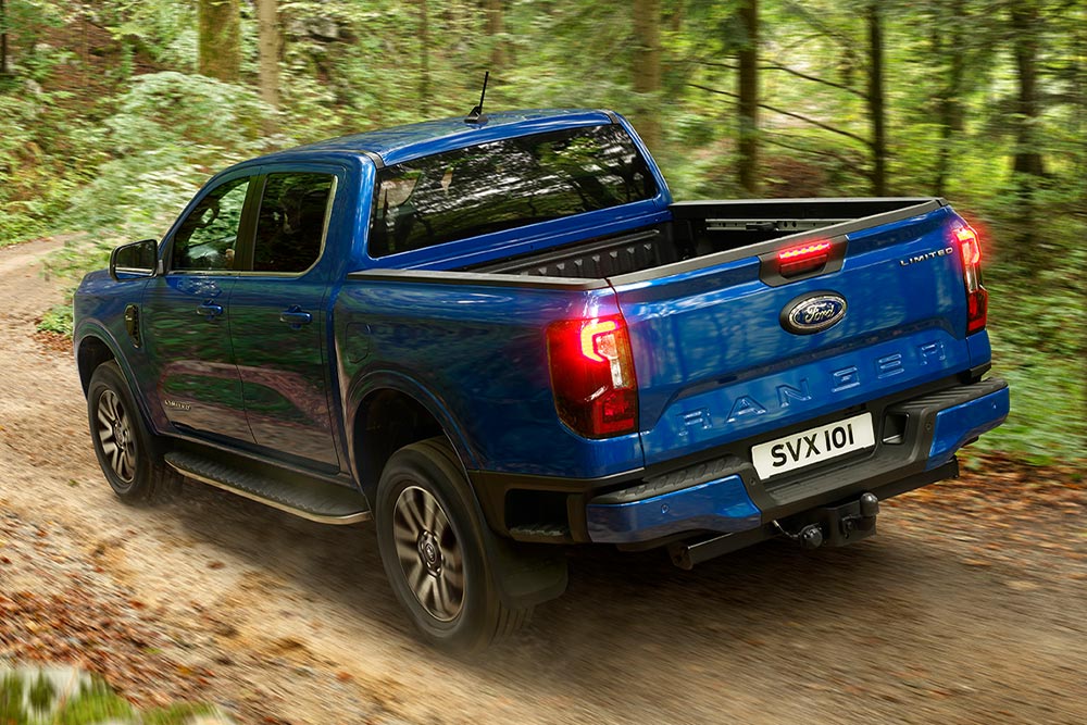 Achterlicht en achterklepaanzicht van een blauwe Ford Ranger pick-up die op een onverharde weg rijdt.