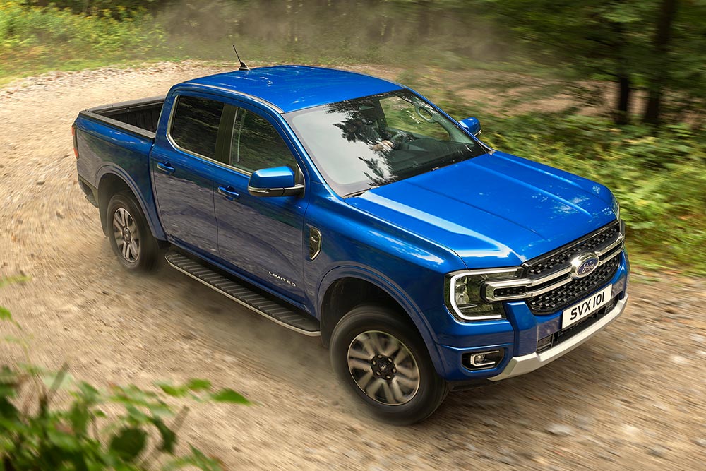 Een blauwe Ford Ranger pick-uptruck rijdt over een onverharde weg door een bos en laat een spoor van stof achter.