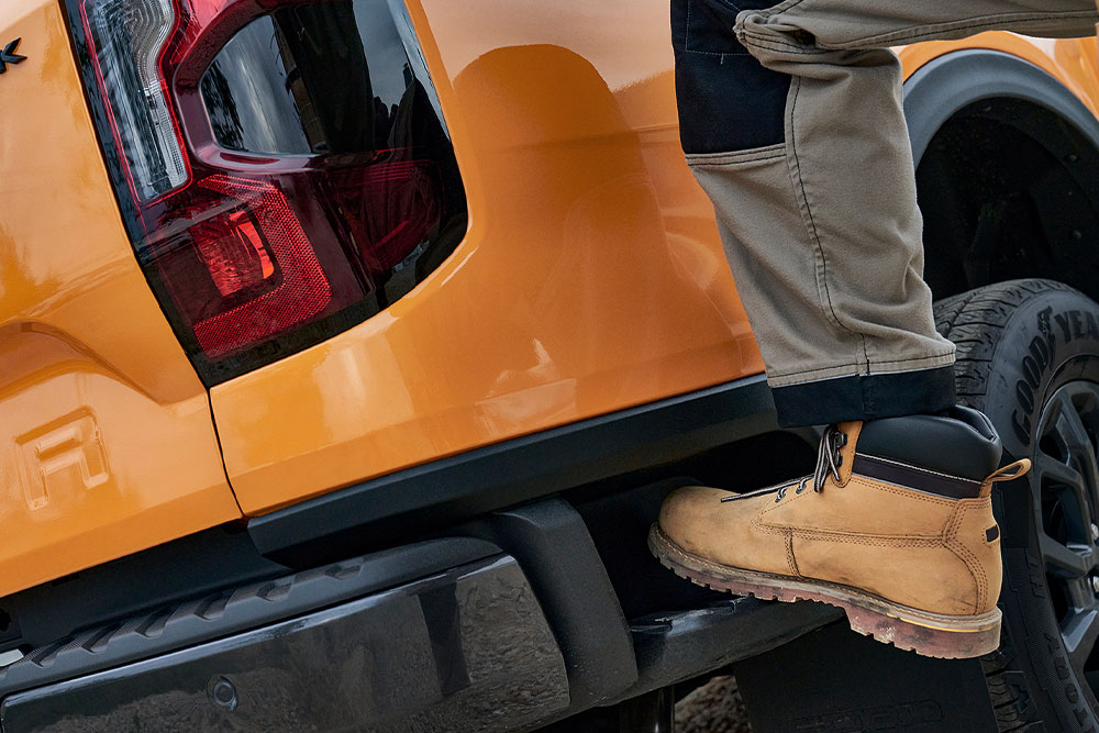 Een bouwvakker die op de geïntegreerde achterste trede van de Ford Ranger stapt.