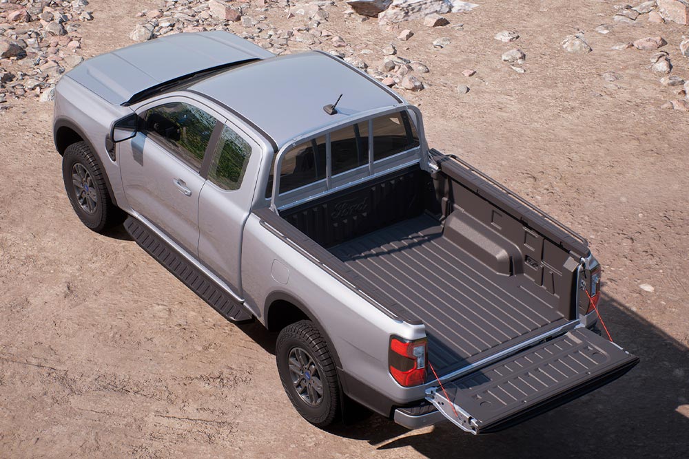 Zilveren Ford Ranger XLT met supercabine geparkeerd op een zandweg met open achterklep, gezien van bovenaf.