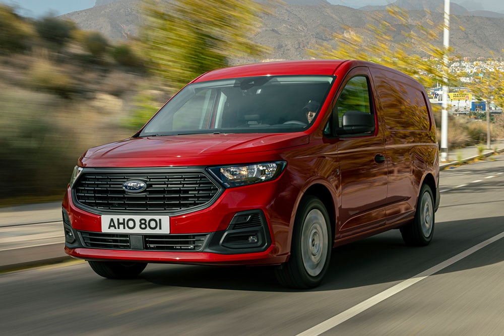 Een Ford Transit Connect rijdend op een weg, met de grille voor en automatische koplampen.