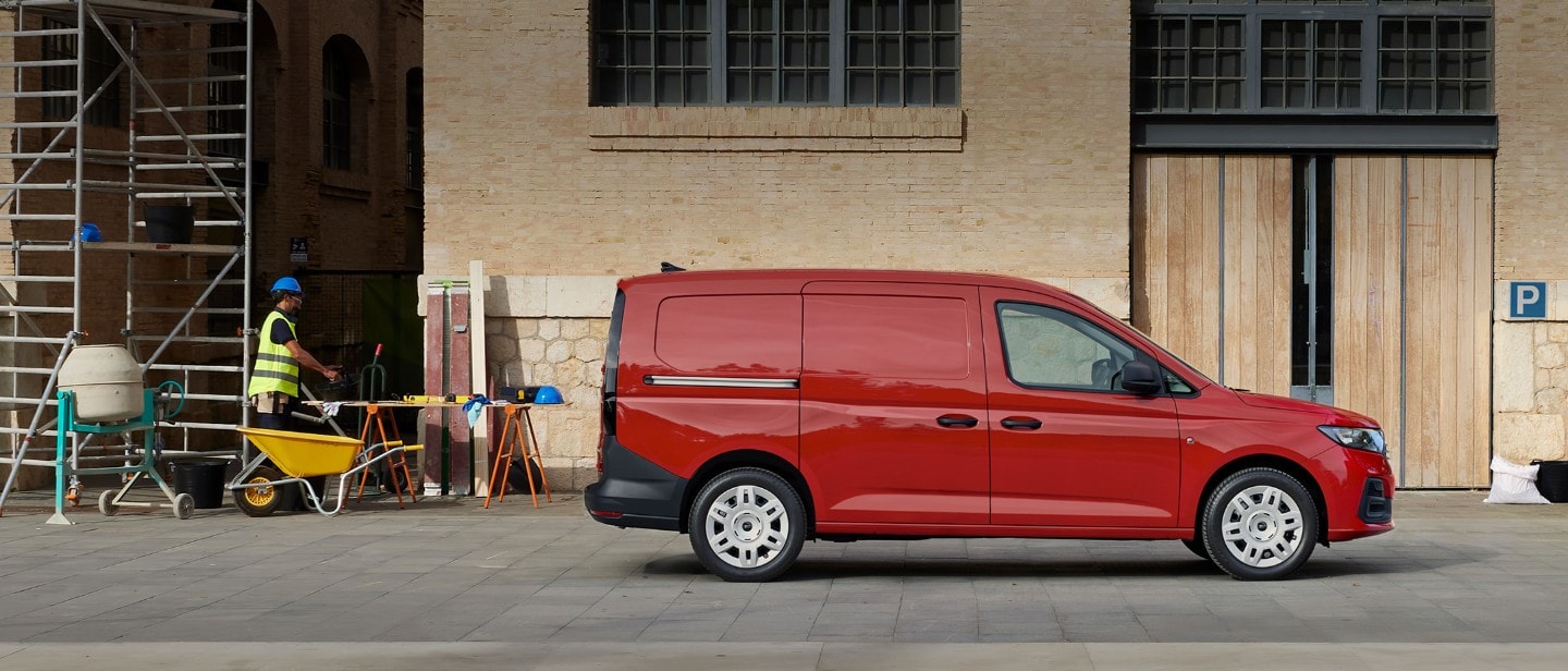 De nieuwe Ford Transit Connect in Maple Red met laaddeur aan de zijkant, geparkeerd bij een bouwplaats.