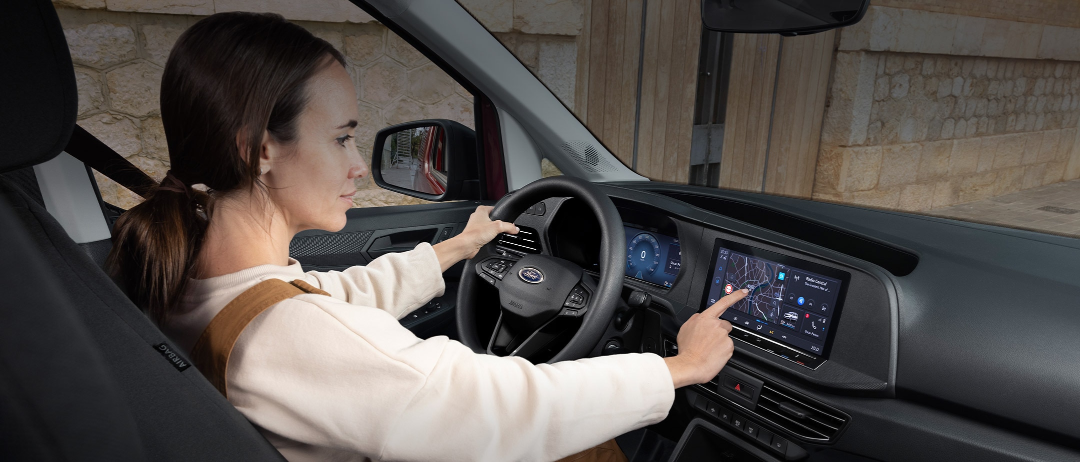 Een vrouw raakt het 10 inch touchscreen aan terwijl ze op de bestuurdersstoel van de nieuwe Ford Transit Connect zit.