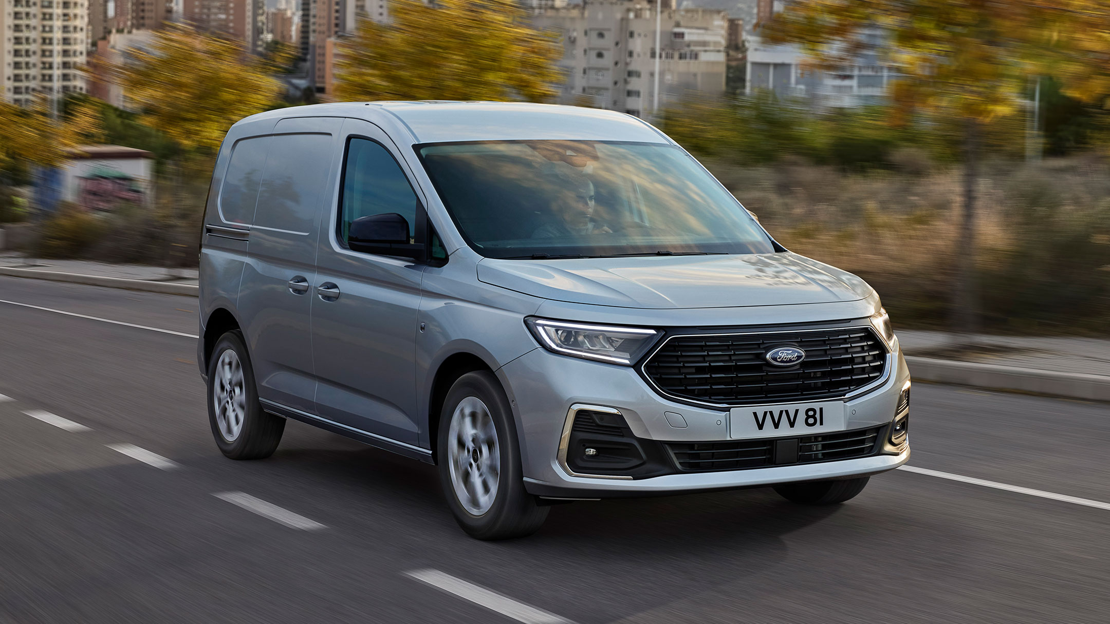 Nieuwe Ford Transit Connect Limited in Stardust Silver rijdend op een weg, met verchroomde buitenkant en automatische koplampen. 