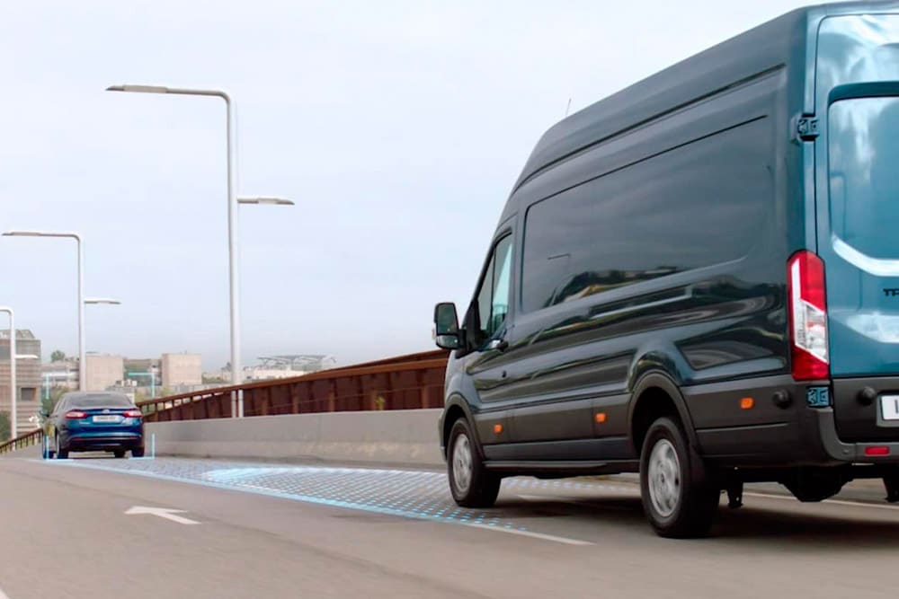 Een blauwe Ford Transit-bestelwagen met blauwe strepen op de weg die het gebruik van de geavanceerde rijhulpsystemen illustreren.