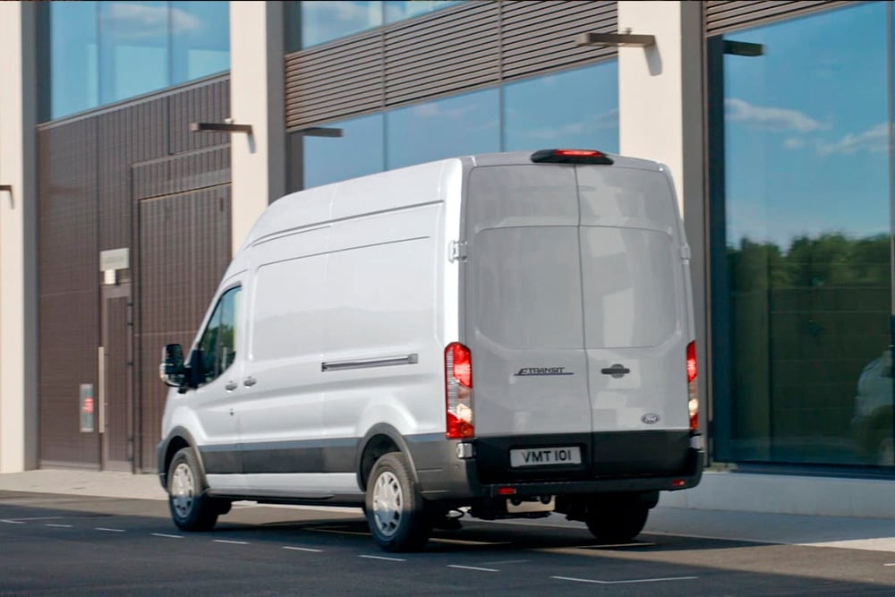 Achterkant van een zilverkleurige Ford Transit-bestelwagen die op een straat in de stad straat geparkeerd staat. 