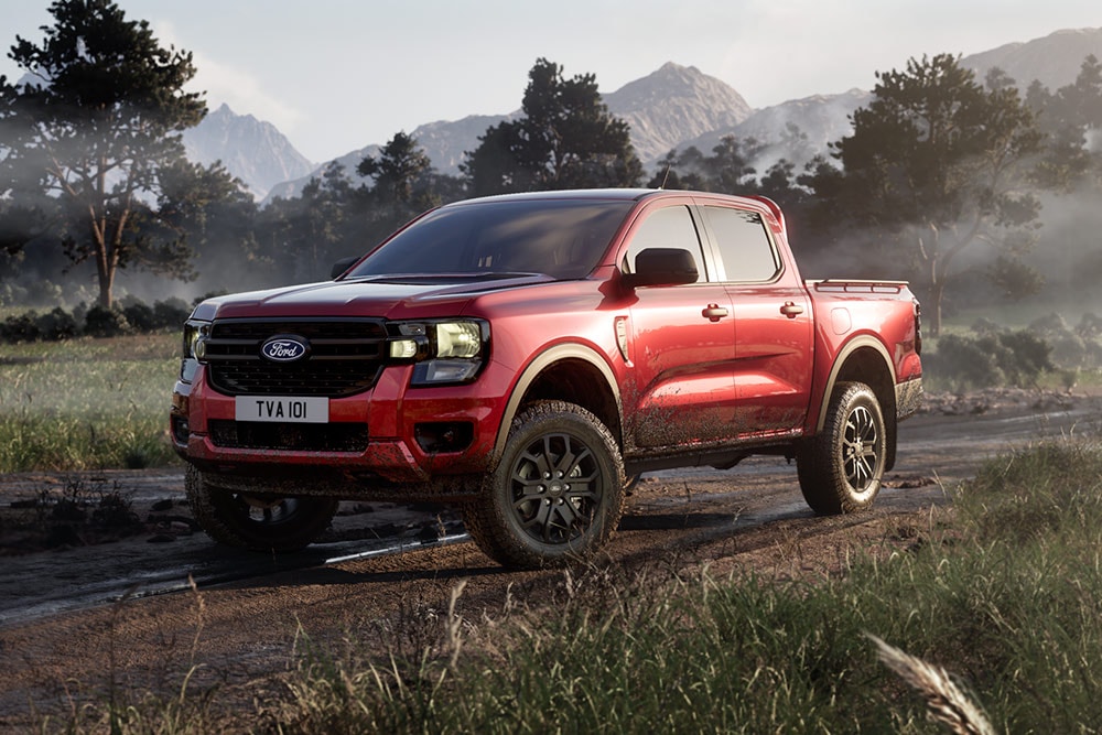 Een rode Ford Ranger Raptor die over een onverharde weg door een weids landschap rijdt.