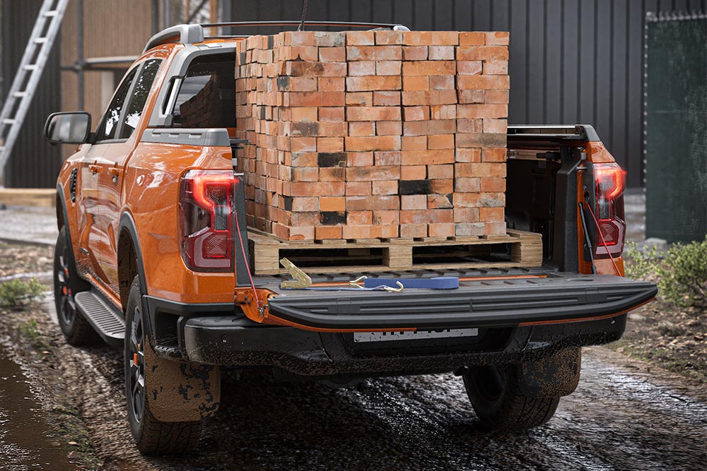 Achteraanzicht van een oranje Ford Ranger, met een stapel stenen in de laadbak.