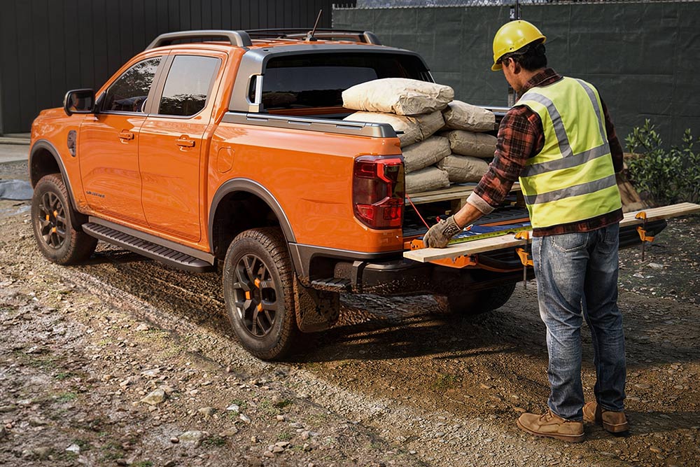 Een bouwvakker die materiaal in de laadbak van een oranje Ford Ranger legt.