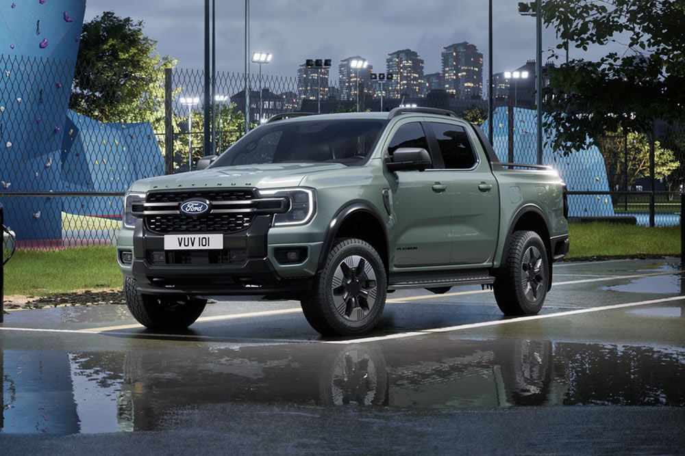 Een grijze Ford Ranger PHEV die bij schemering voor een stedelijke skyline geparkeerd staat.