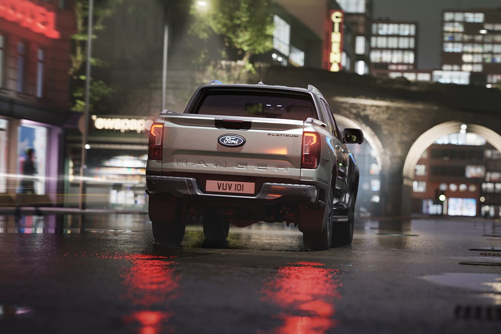Achteraanzicht van een zilverkleurige Ford Ranger die ’s nachts door een neonverlichte stad rijdt.