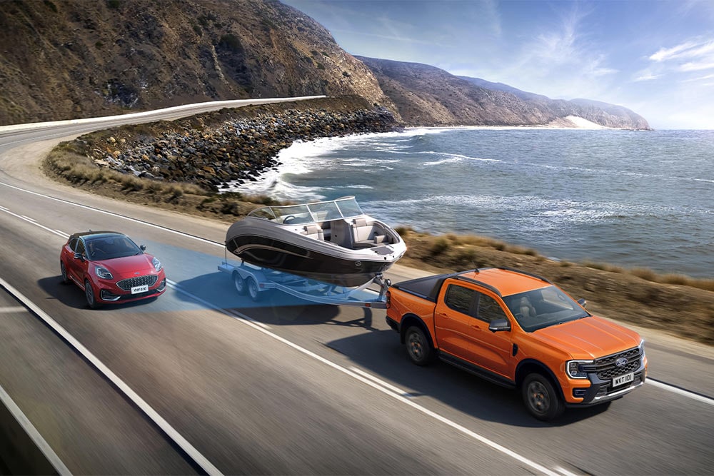 Een oranje Ford Ranger trekt een boot over een kustweg en laat daarmee zijn trekvermogen zien.