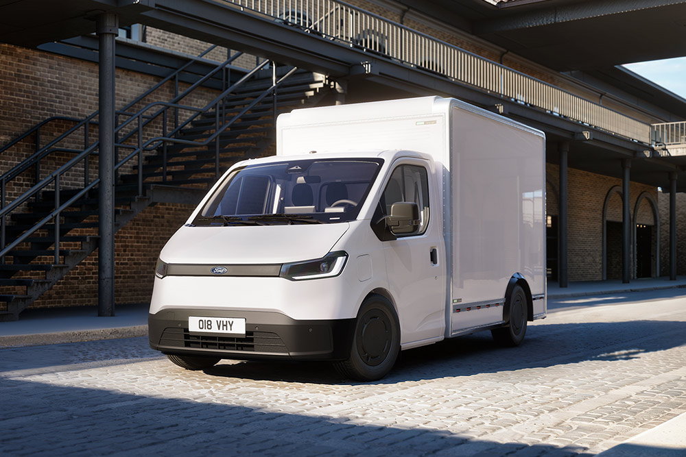 Een witte Ford Transit City® Chassis Cabine-bestelwagen staat geparkeerd voor een bakstenen gebouw.
