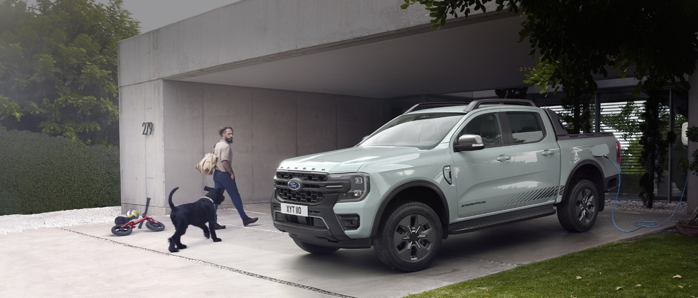 Man met hond loopt langs een Ford Ranger Stormtrak PHEV, aan een oplader