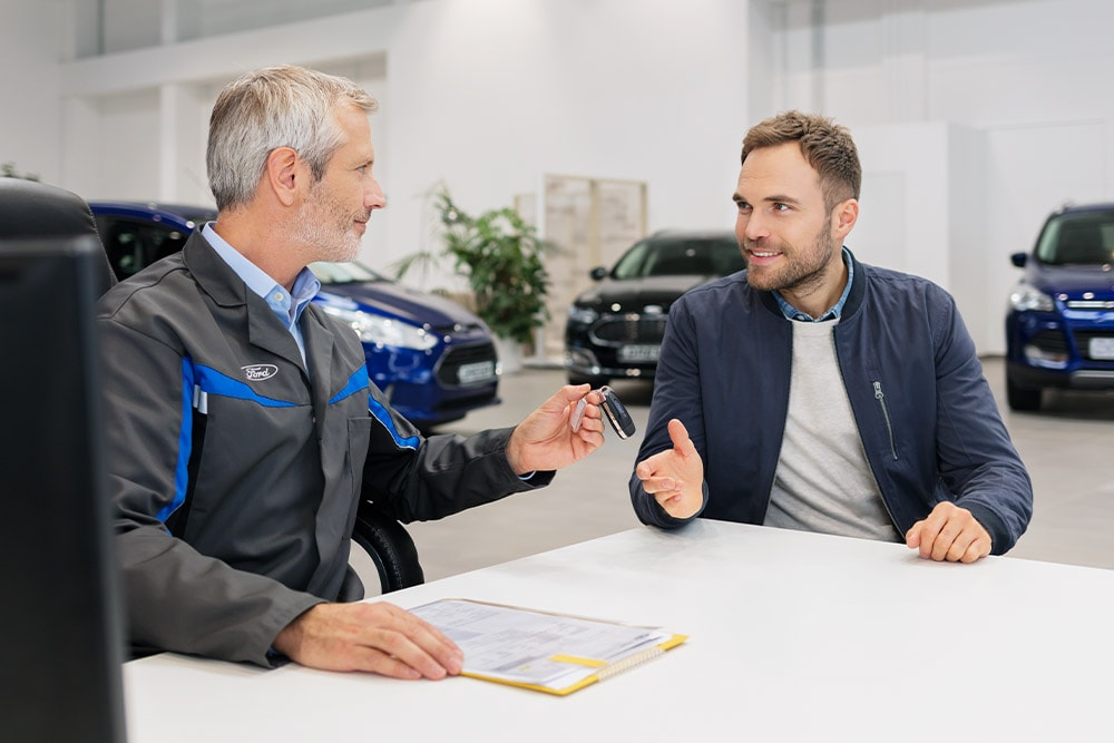 Twee mannen zitten tegenover elkaar bij een Ford-dealer.